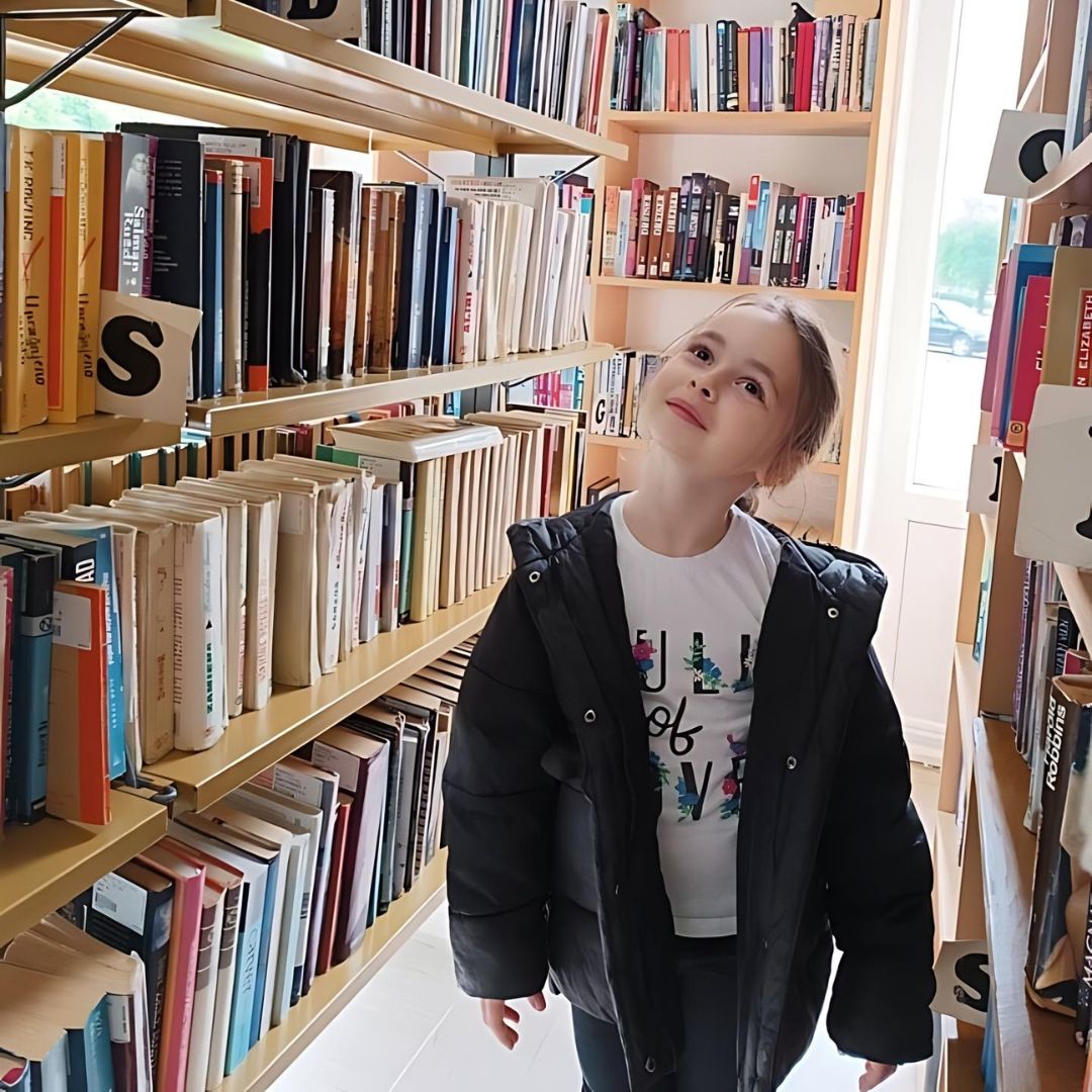 Djevojčica Vrtića Ću-Ću bira knjigu među policama biblioteke